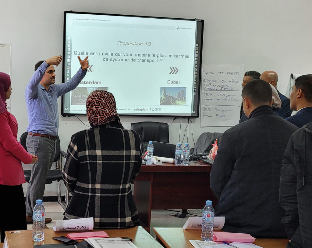 Plusieurs personnes de dos, suivant une formation dans une salle devant un tableau blanc.